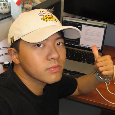 Houfu Chen in a Tim Hortons cap, giving a thumbs up at a desk